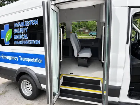 Open curbside passenger door with yellow-edged steps, grab rails and a passenger seat inside
