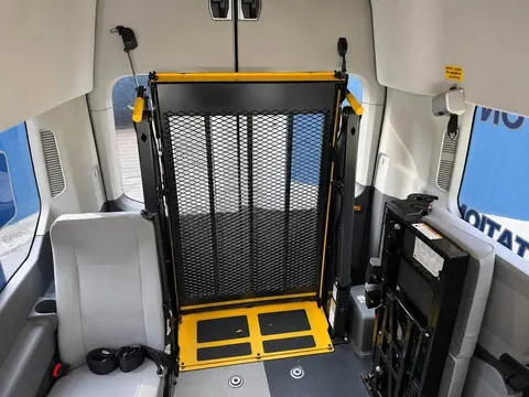 Interior view toward the rear with the lift folded, a passenger seat, wheelchair securement straps and a wheelchair securement location label