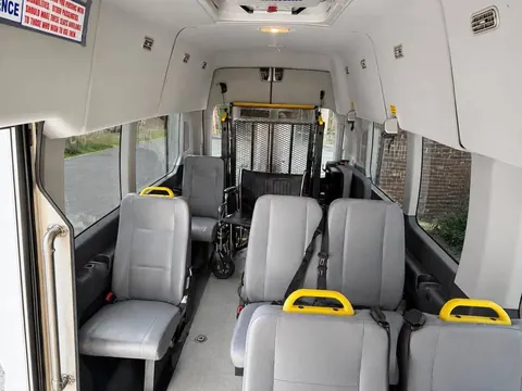 Passenger cabin with gray forward-facing seats and yellow grab handles, a wheelchair at the rear near the lift